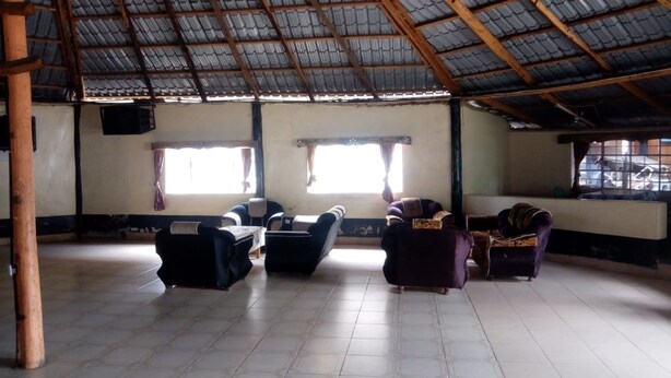 A spacious room with a high ceiling and tiled floor, featuring several sofas and chairs arranged for seating. - Queens Village Hotel (Nakuru)