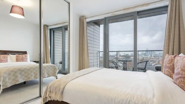Ett hotellrum med en stor säng, en spegel, en balkong med utsikt över staden och ett litet bord.