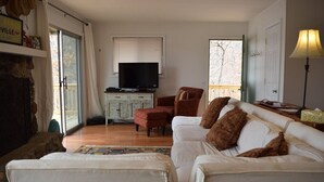 Un salón con sofá blanco, una silla roja con estampado, un televisor sobre un mueble bajo y una lámpara en una mesita auxiliar.