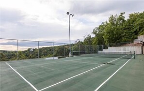 Ein Tennisplatz im Freien mit Netz, umgeben von einem Metallzaun, und eine Straßenlaterne in der Mitte.