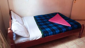 Una cama individual con estructura de madera, una colcha azul y negra a cuadros, una almohada blanca y una toalla rosa doblada.