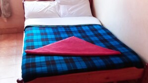 Una cama individual con una colcha azul y roja a cuadros y una almohada rosa.
