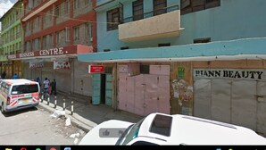 Una calle con coches estacionados y comercios cerrados, incluyendo un centro de negocios y una peluquería.
