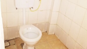 Baño pequeño con azulejos, un inodoro blanco y conexiones de fontanería visibles.