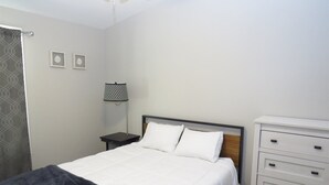 Quarto bem arrumado com cama, mesas de cabeceira, abajur e cômoda.