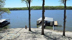 Un muelle con una estructura cubierta, un bote y árboles junto a un lago tranquilo.