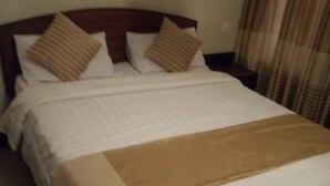 A neatly made bed with white bedding and two brown pillows. - Skyline Hotel & Suites (Nakuru)