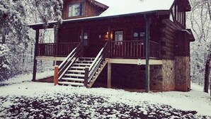 Eine Holzhütte mit Veranda und Treppe, umgeben von schneebedeckten Bäumen.