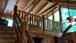 Eine Holztreppe führt zu einem Balkon mit Blick auf Bäume.