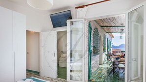 A room with a bed, a bathroom, and a view of a terrace with outdoor furniture.