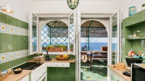 A kitchen with green tiles, a view of the sea, and a dining area with outdoor furniture.