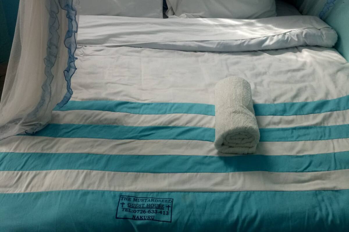 A bed with striped bedding, a rolled towel, and a label with contact information.