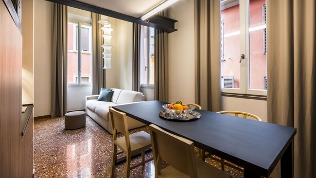 Habitación de hotel compacta con zona de comedor, un sofá y una pequeña mesa con fruta.