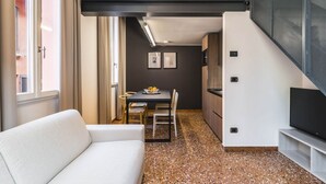 Un espacio habitable compacto con sofá, mesa de comedor con sillas, zona de cocina y televisor.