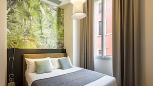 Habitación de hotel con cama, ventana grande con cortinas, lámpara de pared y toma de corriente.