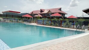 Una piscina con solárium empedrado, rodeada por una valla y edificios con techo rojo.