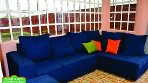 Un sofá azul con cojines verdes y rojos en una habitación con suelo de baldosas y ventanas grandes.