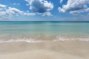 A beach with clear turquoise water and a sandy shore under a partly cloudy sky.