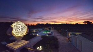 A nighttime view of a resort with a well-lit pathway leading to a pool area, surrounded by landscaped gardens and a clear sky. - La Perla Bianca Luxury Spa by Perle di Puglia (Oria)