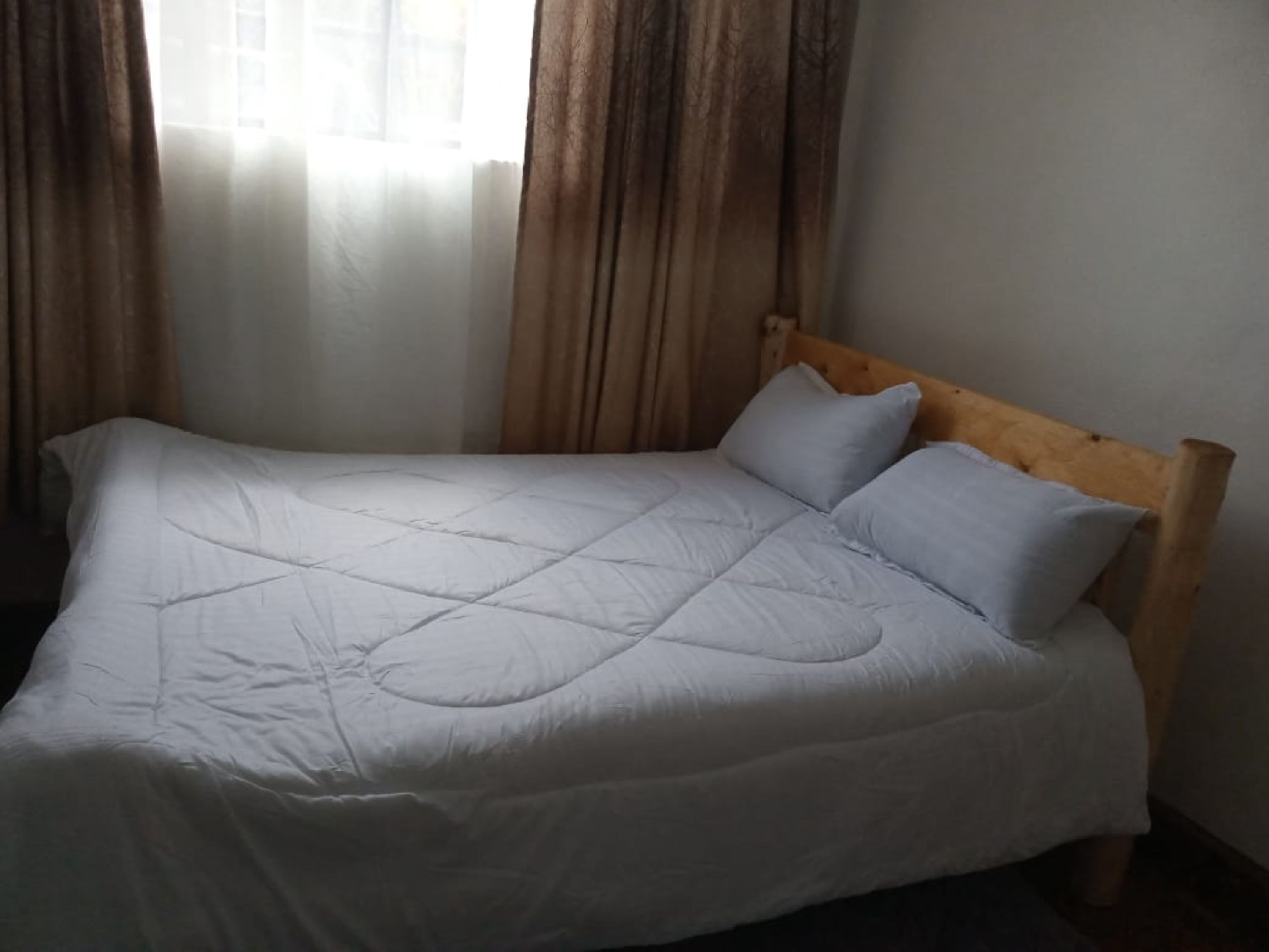 Una cama con cabecera de madera, ropa de cama blanca y una ventana con cortinas.