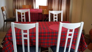 A dining area with a table set for four, surrounded by white chairs, and a window with curtains. - AJ's The Ranch (Nanyuki)