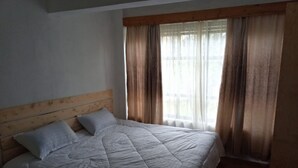 A bedroom with a wooden headboard, a bed with a quilt, two pillows, and a window with curtains. - AJ's The Ranch (Nanyuki)