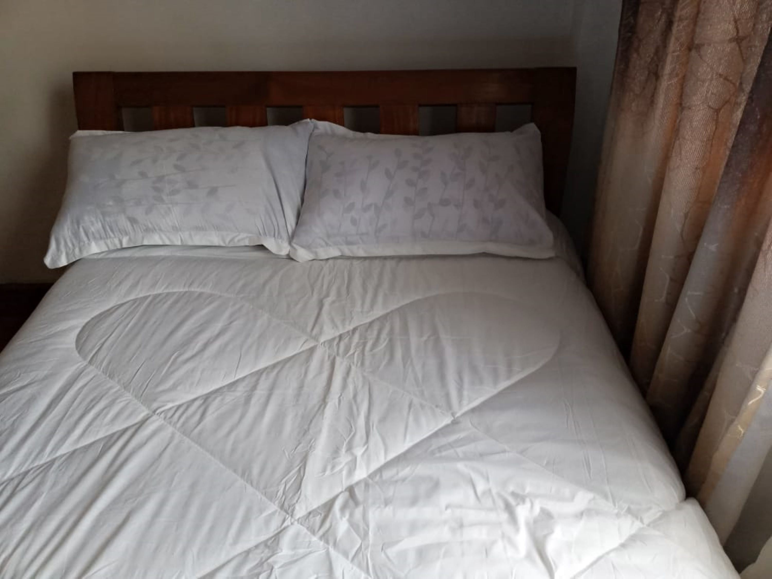 A neatly made bed with a wooden headboard and two pillows.