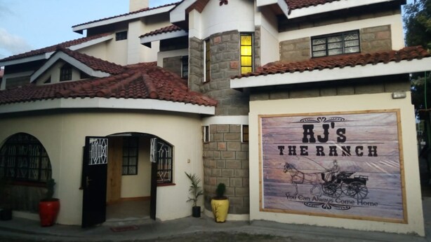 A two-story house with a sign reading "RJ's The Ranch" and a horse-drawn carriage illustration. - AJ's The Ranch (Nanyuki)