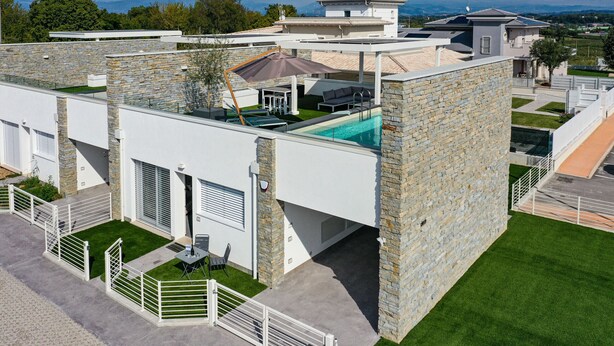 A modern house with a rooftop pool, stone walls, and a well-maintained lawn.