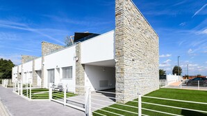 A modern building with stone and white facades, a paved walkway, and green artificial grass.