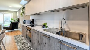 A modern kitchen with light wood cabinets, a stainless steel sink, and a coffee maker.
