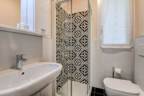 A bathroom with a white sink, a glass shower enclosure, a toilet, and patterned tiles.