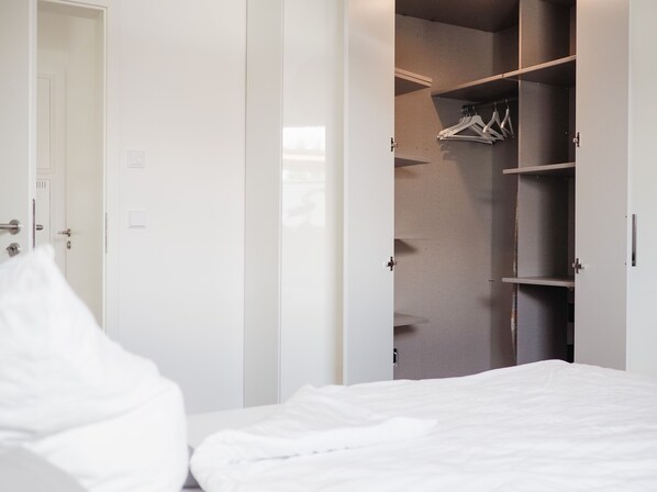 A bedroom with a bed, white walls, and a walk-in closet with hanging space. - Modern vacation apartment with a lake view and a terrace (Großräschen)