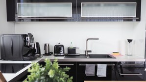 Una cuina moderna amb armaris negres, un vàter d'acer inoxidable, una màquina de cafè, una torradora i una planta en test.