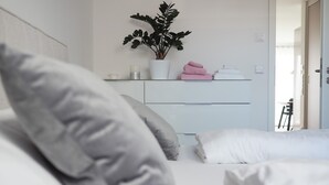 Un dormitori amb un llit, almoines, una taula de nit amb una planta, i una porta que dona a una altra habitació.