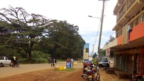 Uma estrada de terra com motocicletas estacionadas no acostamento, uma placa de sinalização e um edifício com fachada vermelha.