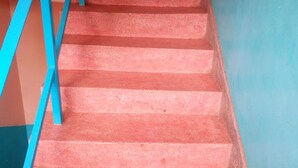 Escada com degraus vermelhos e guarda-corpos azuis, subindo para um andar superior.