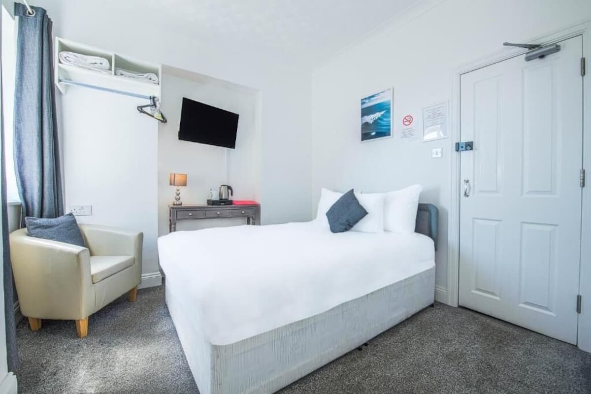 Habitación de hotel con cama, una silla, televisor, escritorio con lámpara y una puerta.
