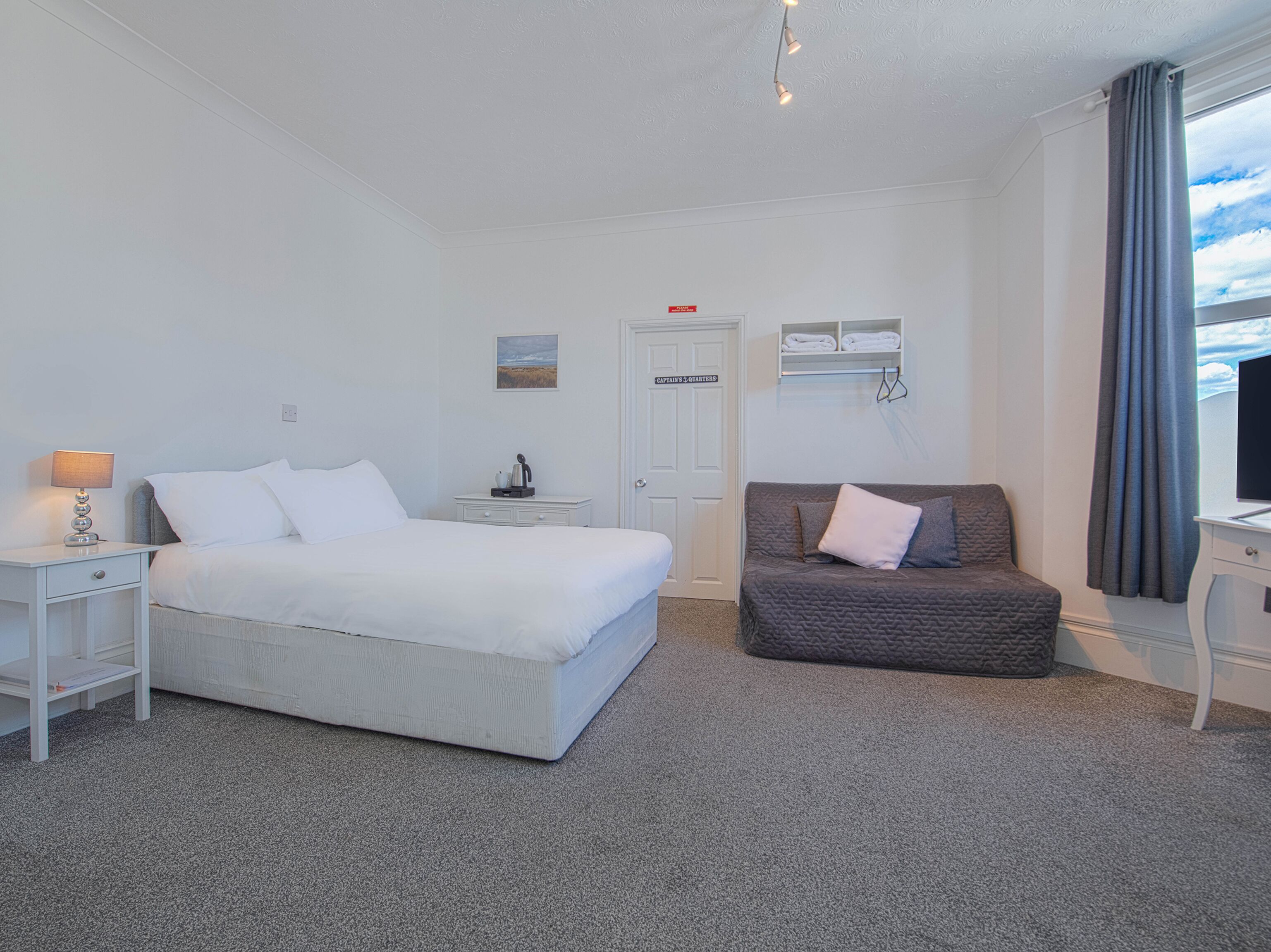 Habitación de hotel con cama, silla, escritorio, lámpara, televisión, puerta y ventana con cortinas.