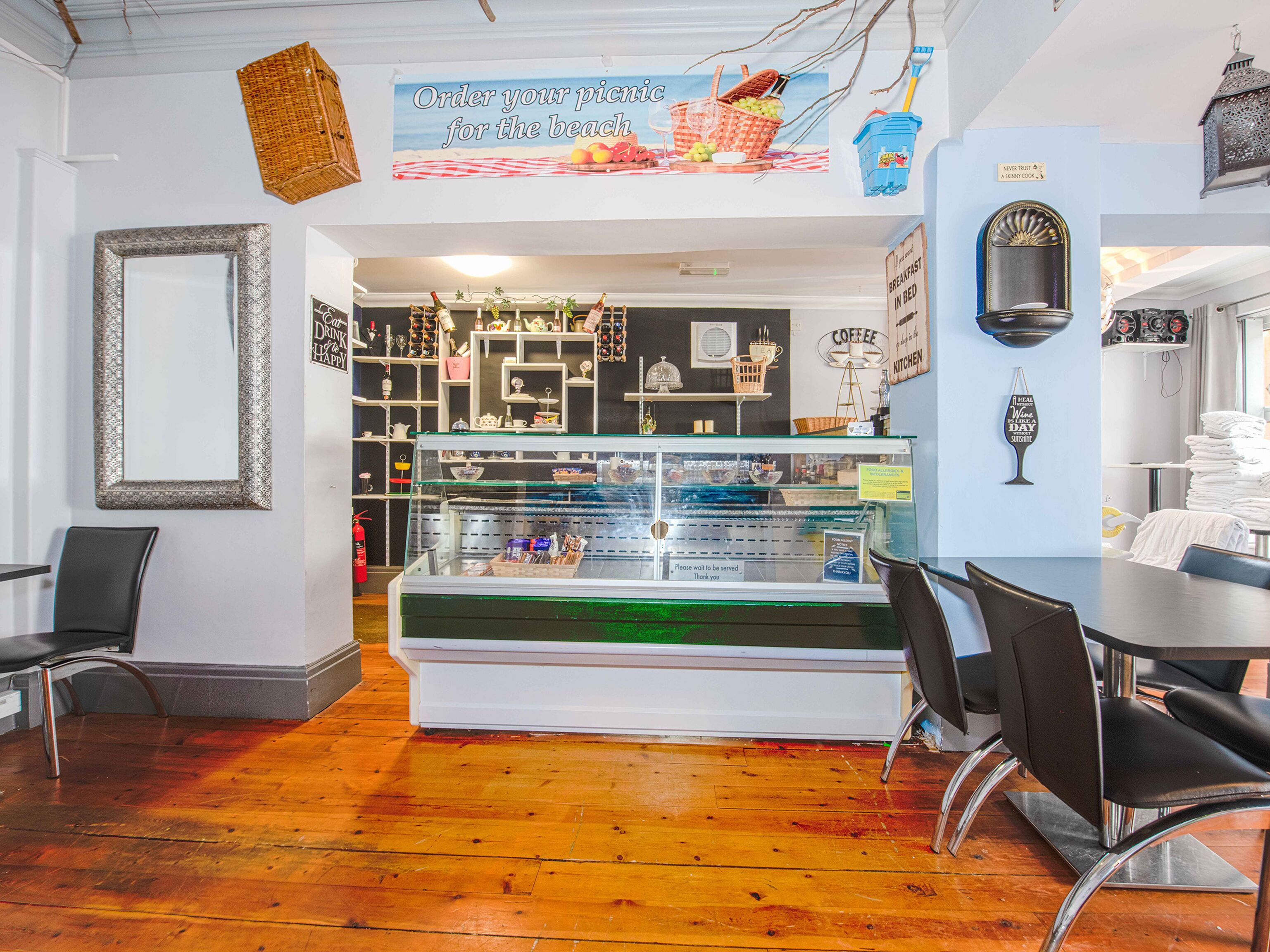 A cafe with a glass display case, wooden flooring, and a beach-themed sign.