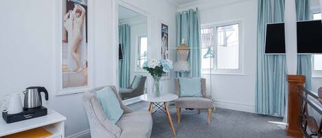 A room with a white cabinet, a table with a vase, two chairs, a mirror, and a window with curtains.