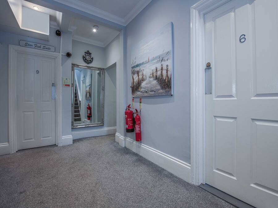 A hallway with a Star Fish Suite sign, a fire extinguisher, a painting, and a door with the number 6.