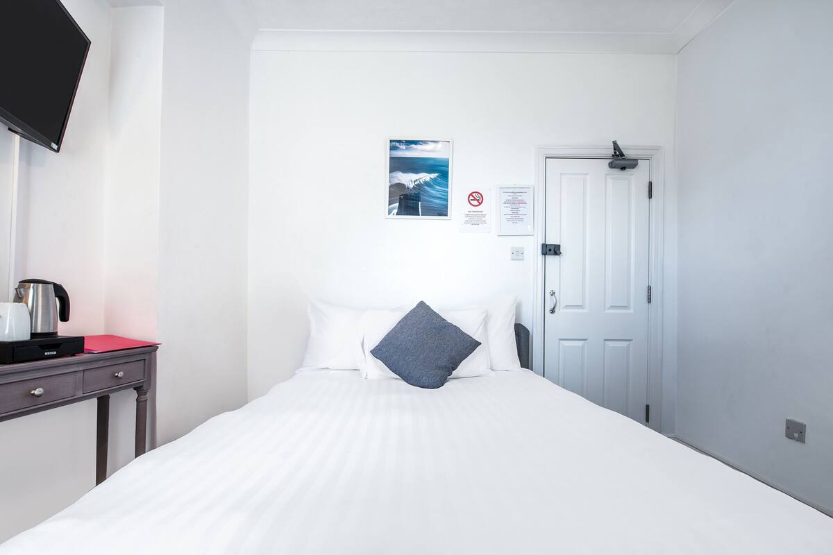 Habitación de hotel con cama, escritorio con hervidor, televisión de pantalla plana, puerta y un cartel en la pared.