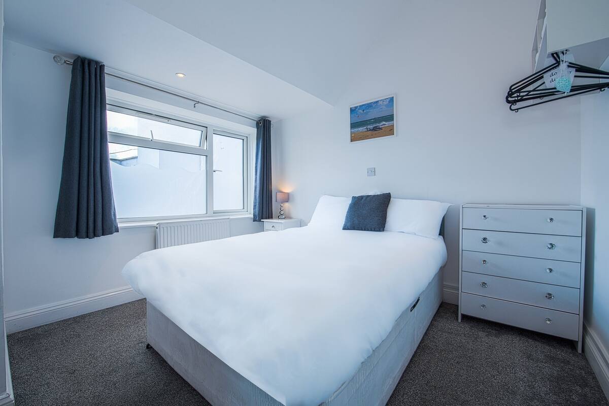 Un dormitorio con cama, cómoda, ventana con cortinas, lámpara de pared y una pintura de playa.