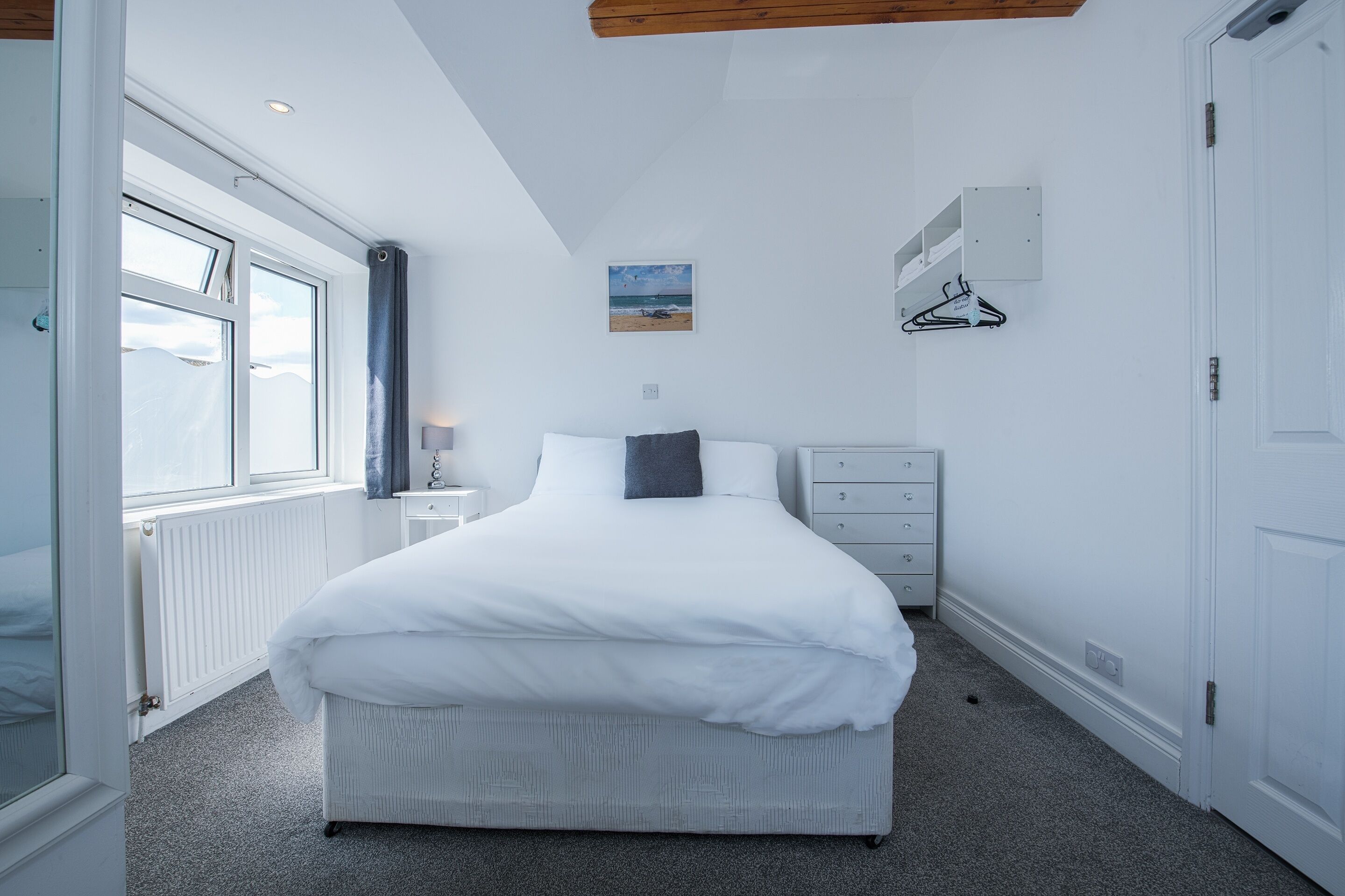A bedroom with a bed, a dresser, a nightstand, a window, and a wall-mounted picture.