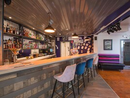 En bar med træloft, en disk med diverse flasker og barstole.