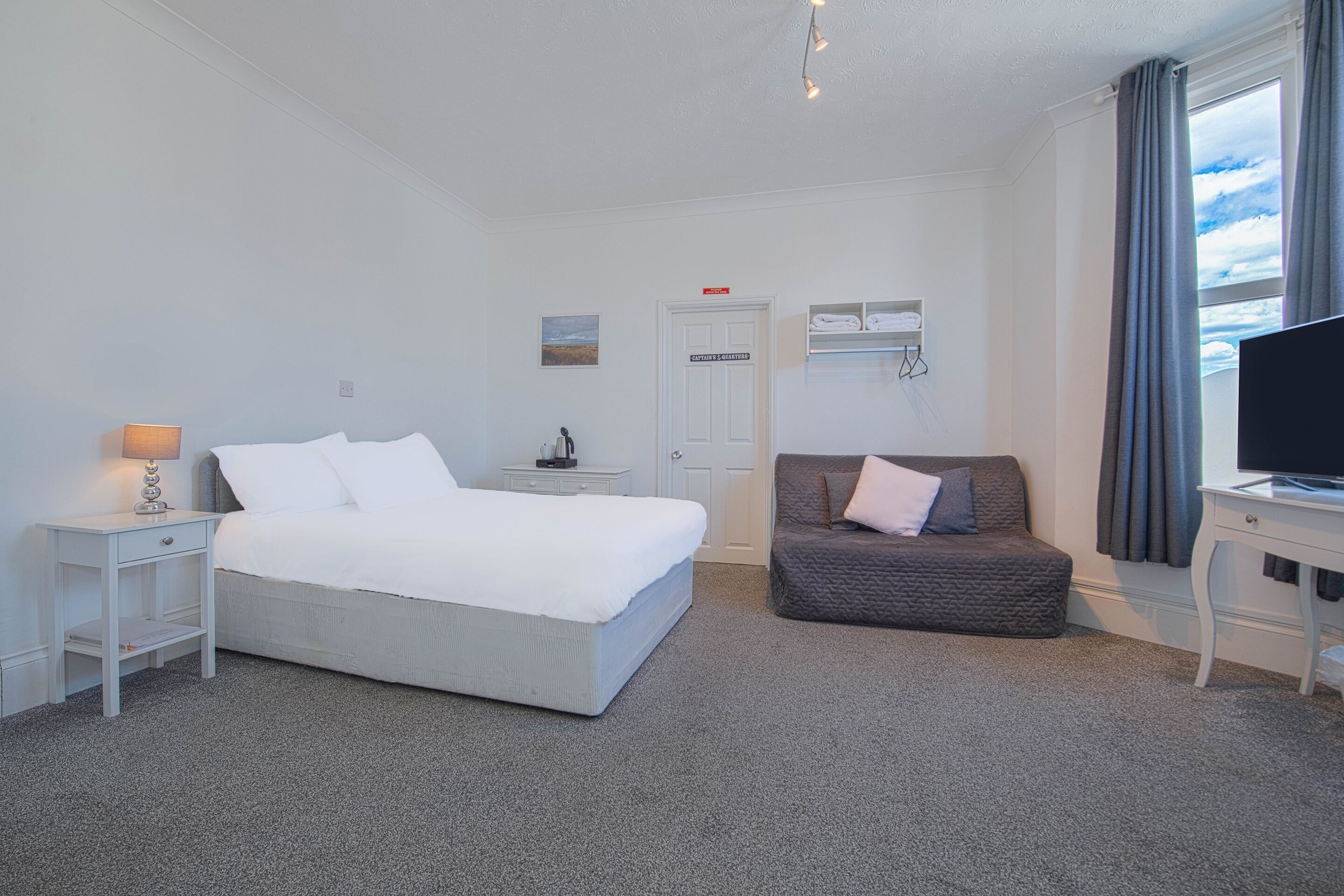 Une chambre d’hôtel comprenant un lit, une table de chevet avec une lampe, un canapé, une télévision et une fenêtre avec des rideaux.