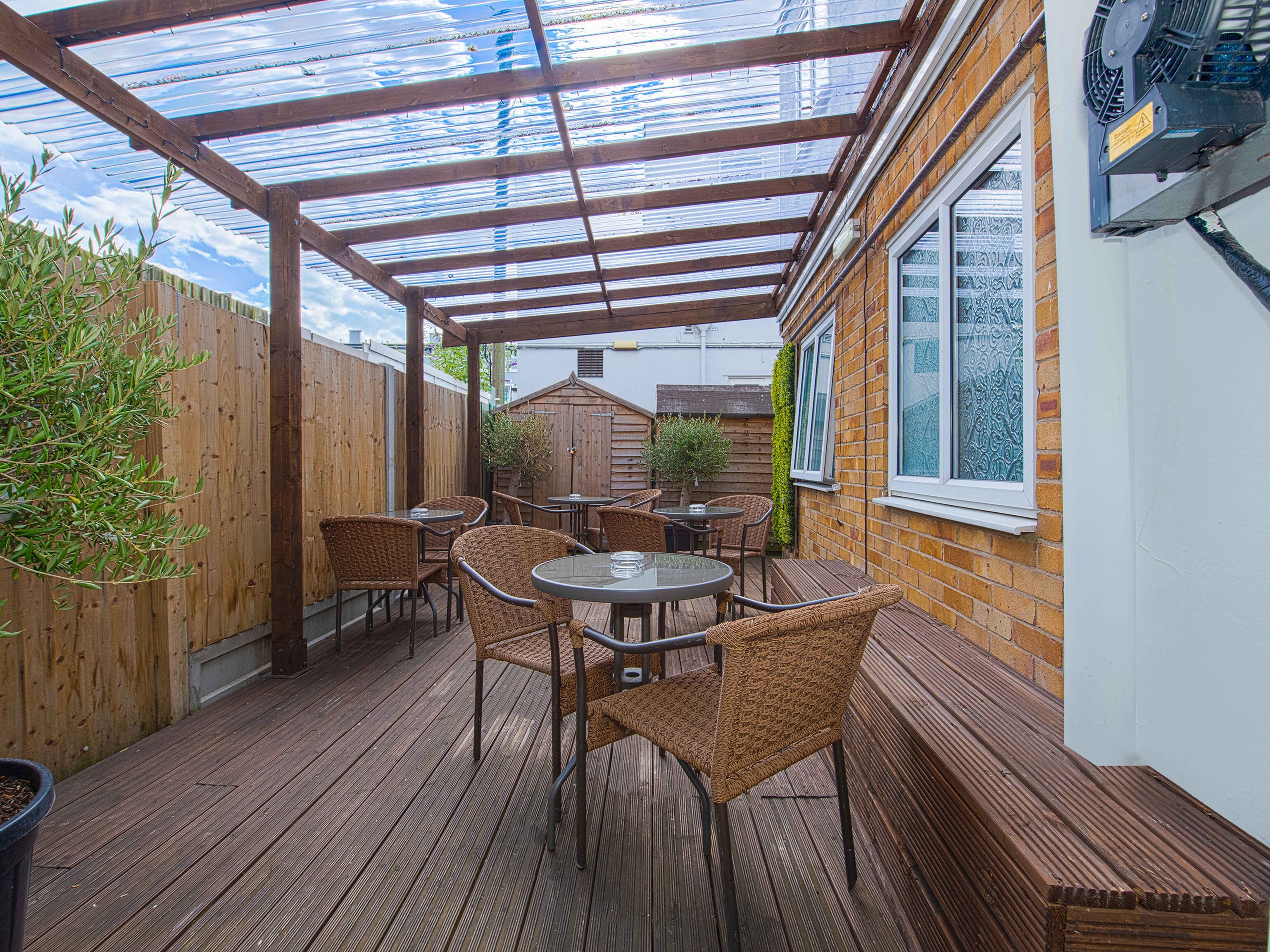 A covered patio area with wooden flooring, wicker furniture, and a glass ceiling.