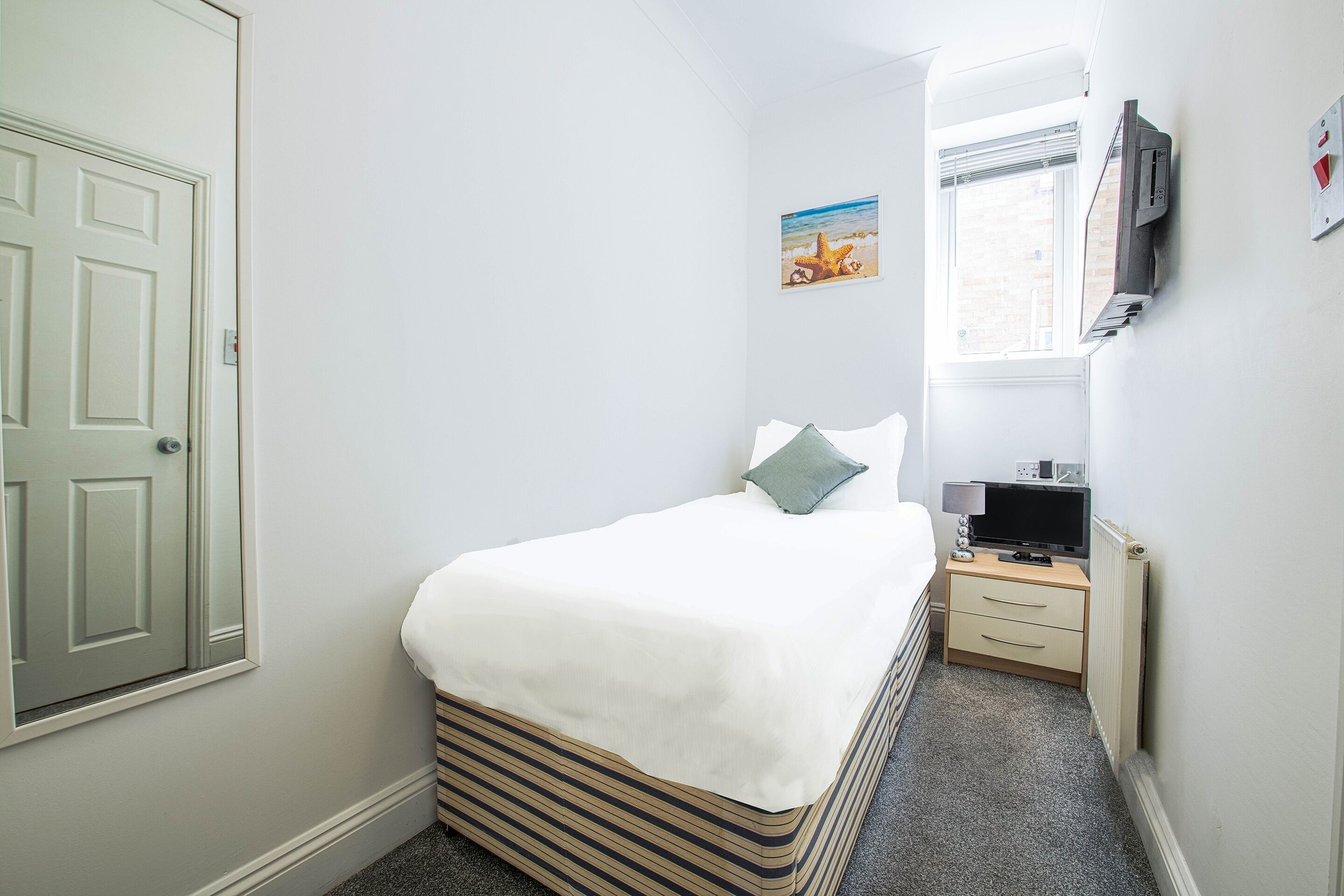 Une chambre à coucher avec un lit, une table de chevet, une télévision et une fenêtre.