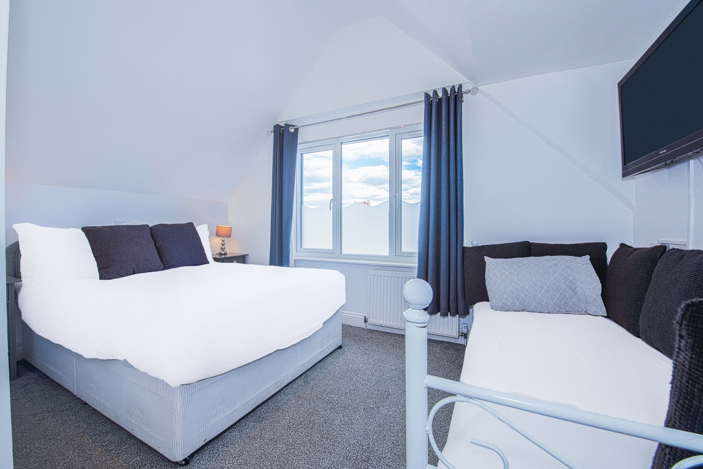 Une chambre d’hôtel avec un grand lit, un plus petit lit, une télévision et une fenêtre avec des rideaux.